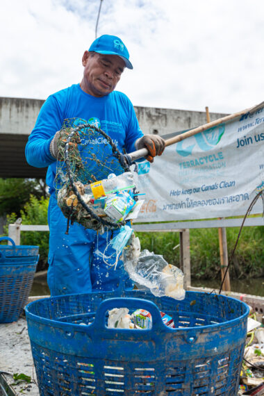 A worker dumps a net full of trash into a basket from the river plastic trap