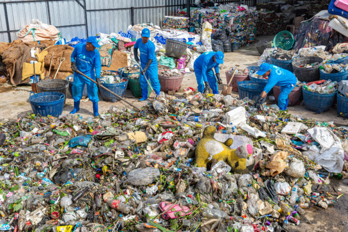 Four workers at the sorting site use tools to separate out the raw trash