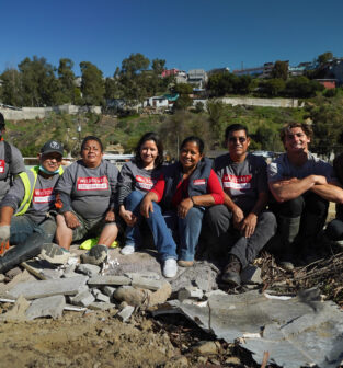 8 members of the WILDCOAST team sitting together and smiling at the camera onsite in Los Laureles Canyon.